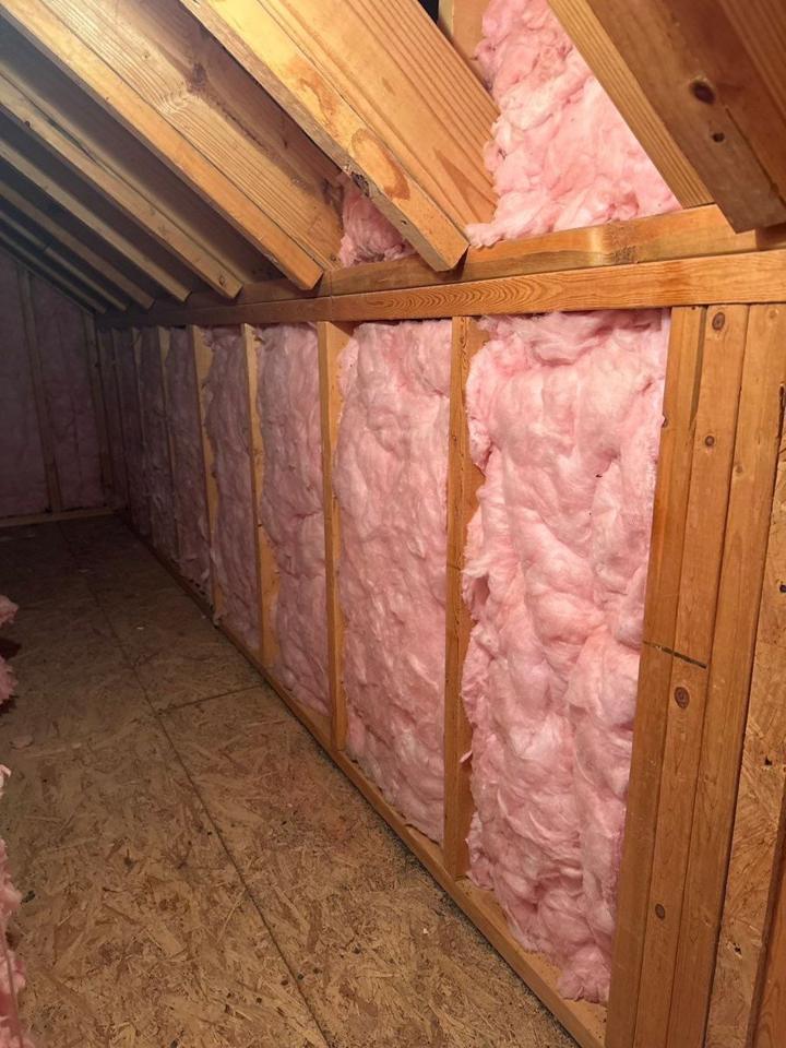 New pink insulation installed between wall studs in a crawl space