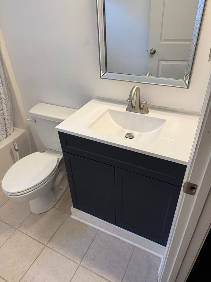 Renovated bathroom with navy vanity, white countertop and new mirror