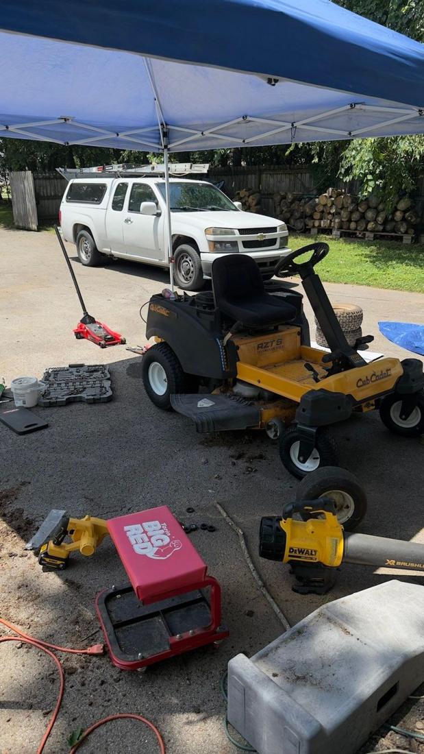 Zero-turn mower being repaired under a canopy